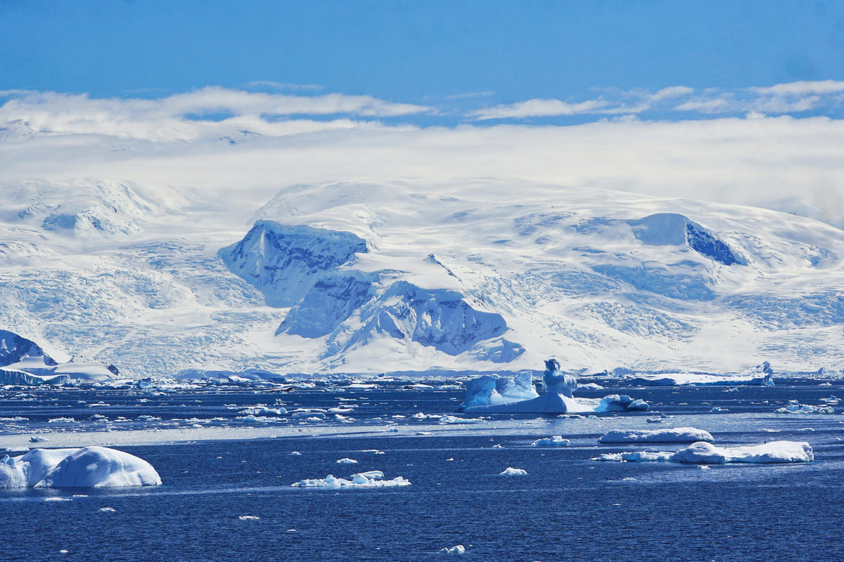 Snow-covered mountains and glaciers across a bay of floating ice in Antarctica.