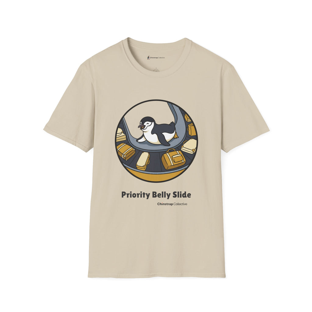 Priority Belly Slide penguin T-shirt in Sand: Inside a round frame, the penguin belly-slides along an airport luggage…