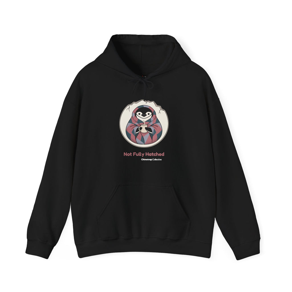 Not Fully Hatched penguin hoodie in Black: Wrapped in a round eggshell white blanket with a jagged cracked rim, the…