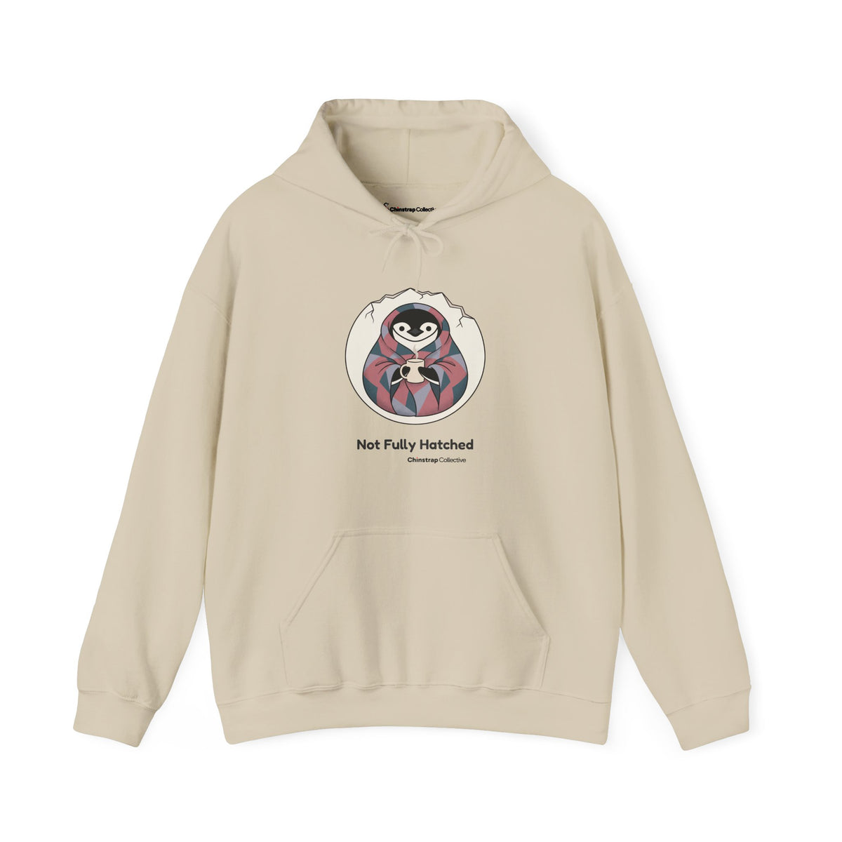 Not Fully Hatched penguin hoodie in Sand: Wrapped in a round eggshell white blanket with a jagged cracked rim, the…