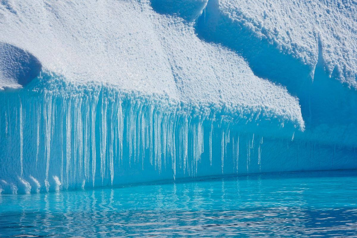 Blue glacier ice with icicles hanging over turquoise water