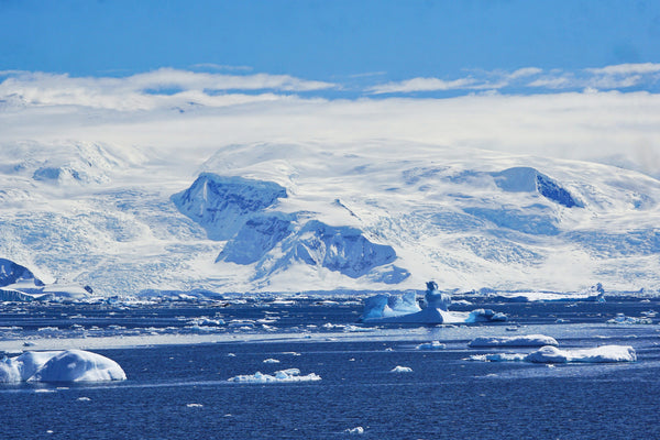 Snow-covered mountains and glaciers across a bay dotted with floating ice