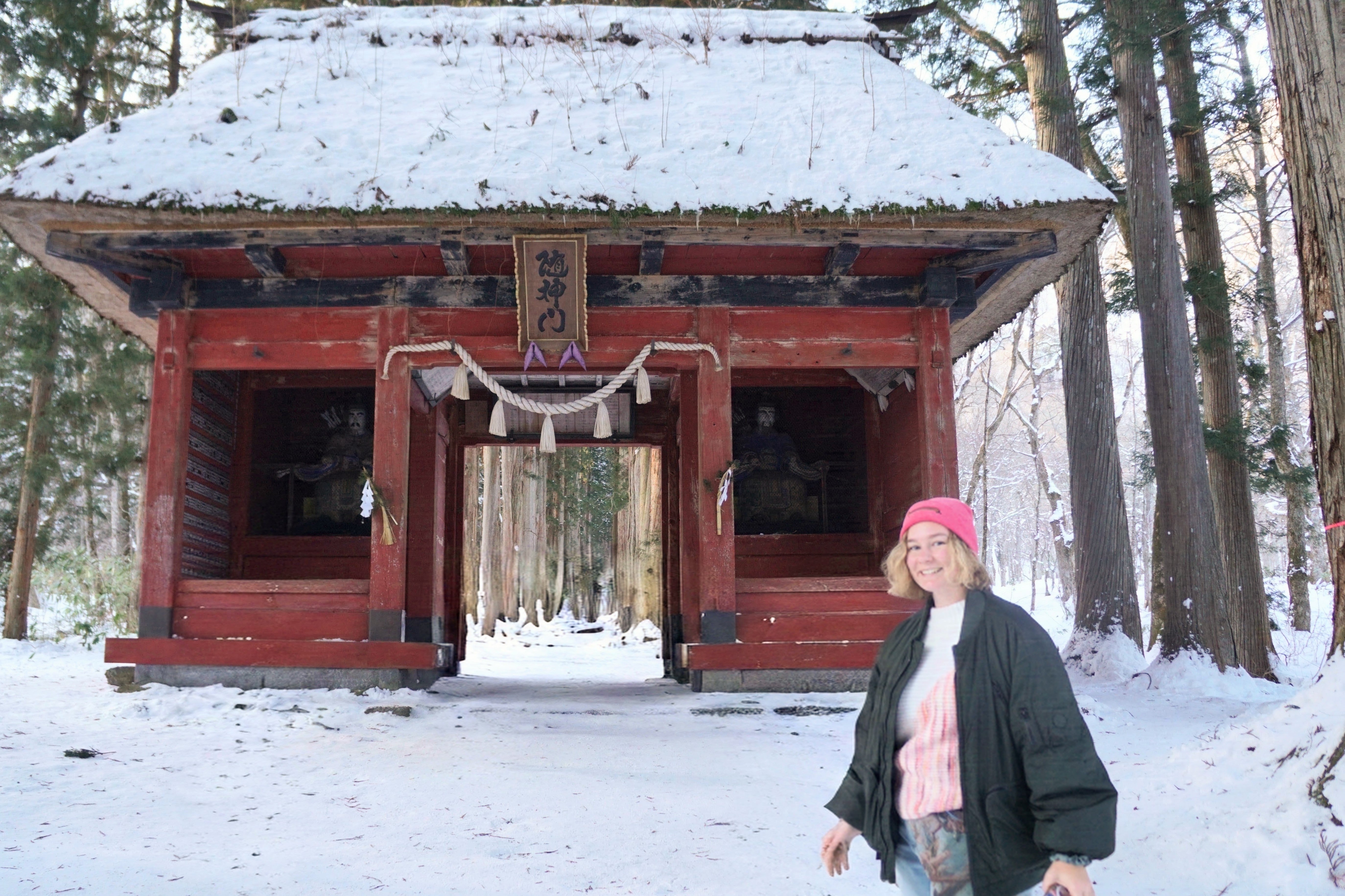 Oli standing in the snow in front of a red wooden shrine gate in a forest